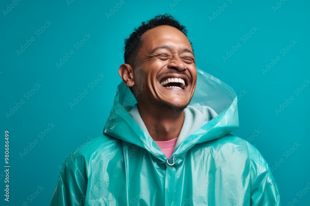 Portrait of a smiling man in his 40s wearing a vibrant raincoat isolated on pastel teal background Portrait of a smiling man in his 40s wearing a vibrant raincoat isolated on pastel teal background