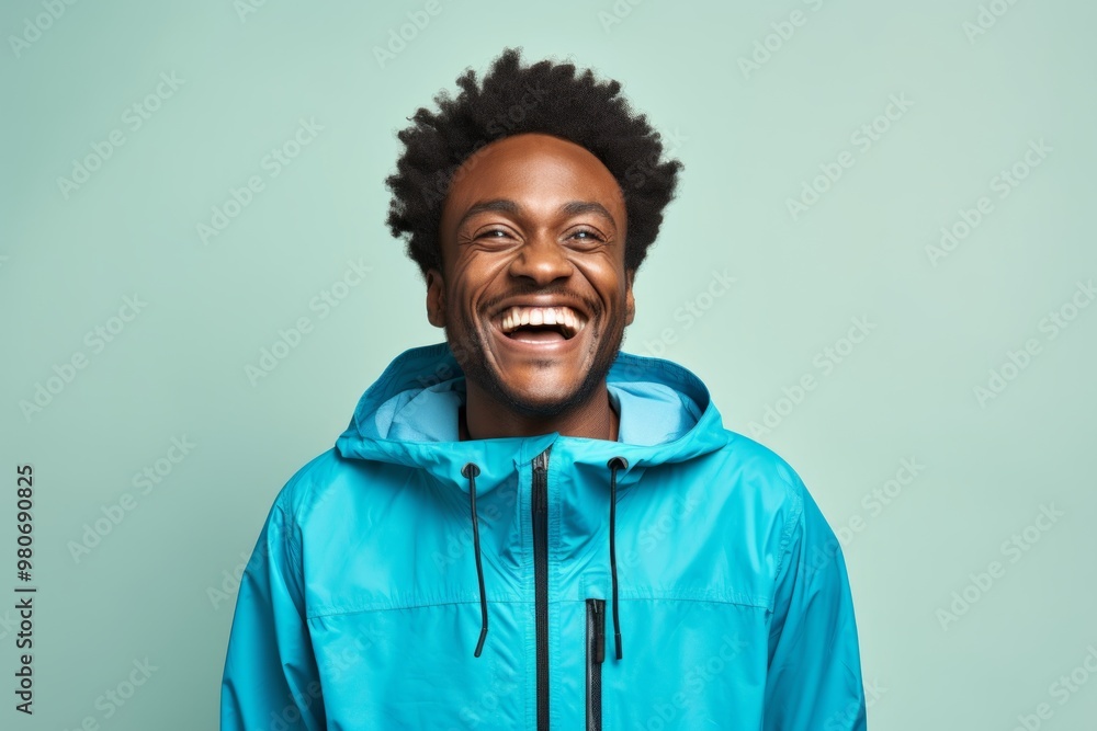 Portrait of a grinning afro-american man in his 30s wearing a lightweight packable anorak over soft blue background Portrait of a grinning afro-american man in his 30s wearing a lightweight packable anorak over soft blue background