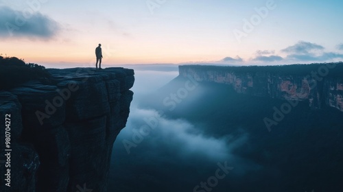 A solitary figure stands on a cliff at sunrise, overlooking a misty valley.