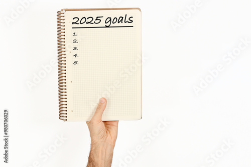 2025 goals written on a notebook held by a man. Isolated on white background.