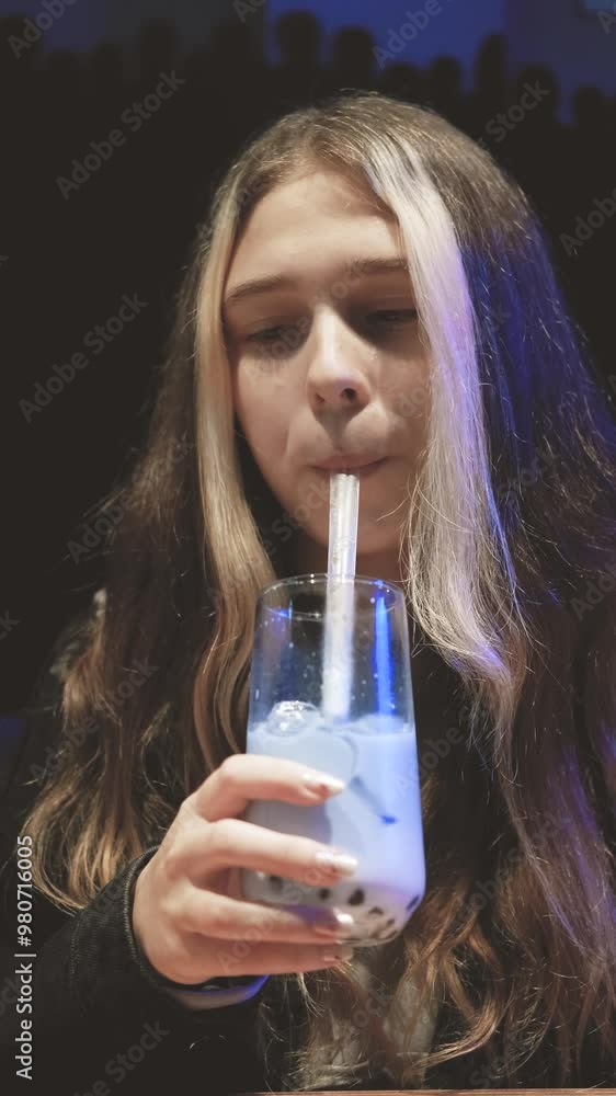 Cute teenage girl with long hair drinking white and blue non-alcoholic cocktail in cafe in the evening Cute teenage girl with long hair drinking white and blue non-alcoholic cocktail in cafe in the evening