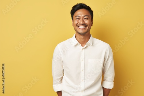 Portrait of a joyful asian man in his 30s wearing a simple cotton shirt on soft yellow background