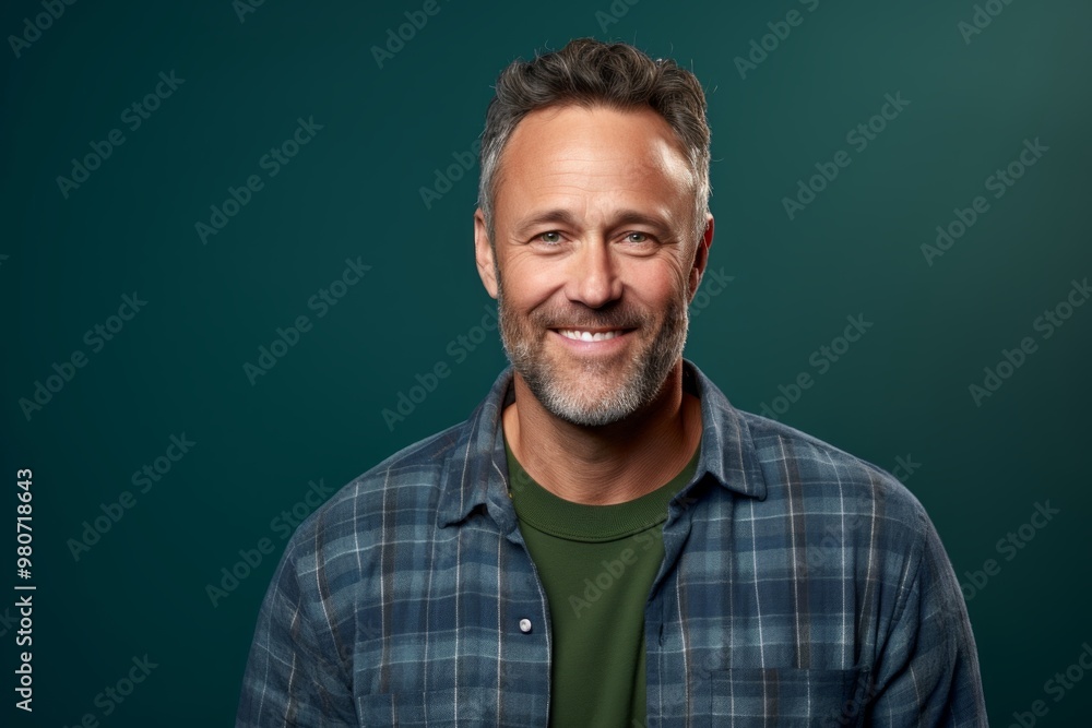 Portrait of a grinning man in his 40s wearing a comfy flannel shirt over soft green background Portrait of a grinning man in his 40s wearing a comfy flannel shirt over soft green background