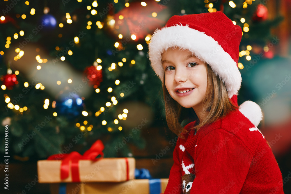 Cute preschool girl in santa hat feeding teddy bear with cookies and milk next to xmas tree Cute preschool girl in santa hat feeding teddy bear with cookies and milk next to xmas tree
