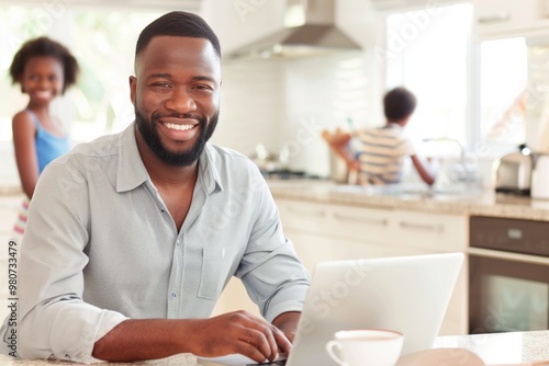 Smiling father working on laptop while children play in modern kitchen