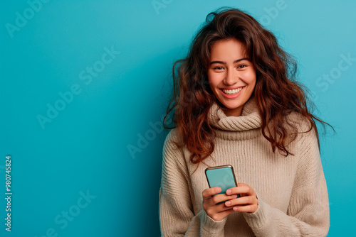 smiling woman looking at her phone, commercial studio photo with plain blue background