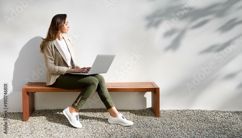 Woman with Laptop in Minimalist Space- A woman working on her laptop, sitting on a minimal bench, with a simple, modern wall in the background