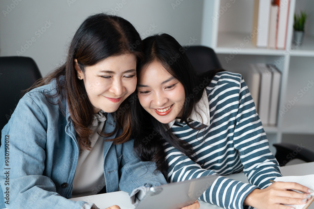 Cheerful woman lying with mother and Enjoying Time Together While Looking at a Tablet in a Modern Office Setting Cheerful woman lying with mother and Enjoying Time Together While Looking at a Tablet in a Modern Office Setting