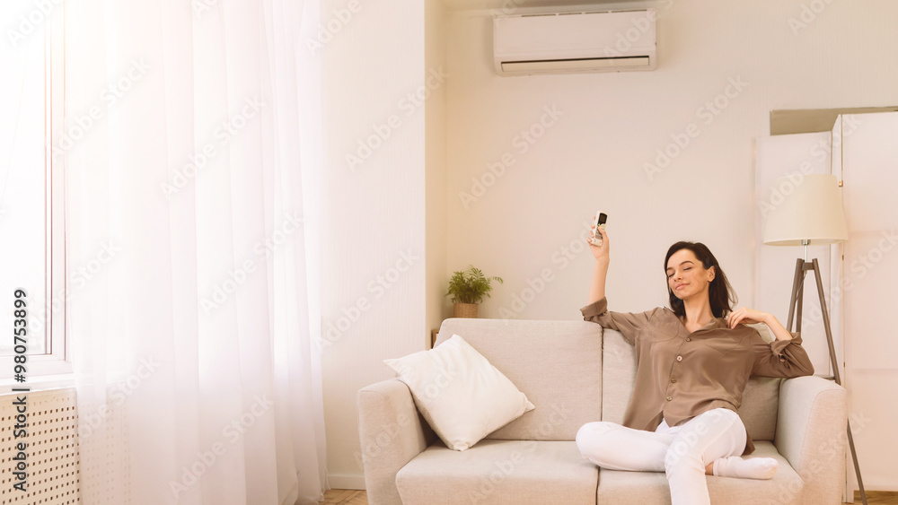 Get Ready For Summer Weather. Calm girl switching on air conditioner relaxing on sofa at home, copyspace Get Ready For Summer Weather. Calm girl switching on air conditioner relaxing on sofa at home, copyspace