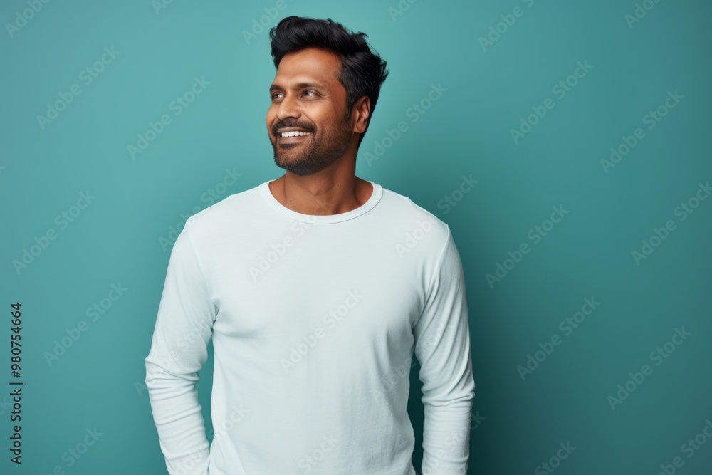 Portrait of a satisfied indian man in his 30s sporting a long-sleeved thermal undershirt in soft teal background Portrait of a satisfied indian man in his 30s sporting a long-sleeved thermal undershirt in soft teal background