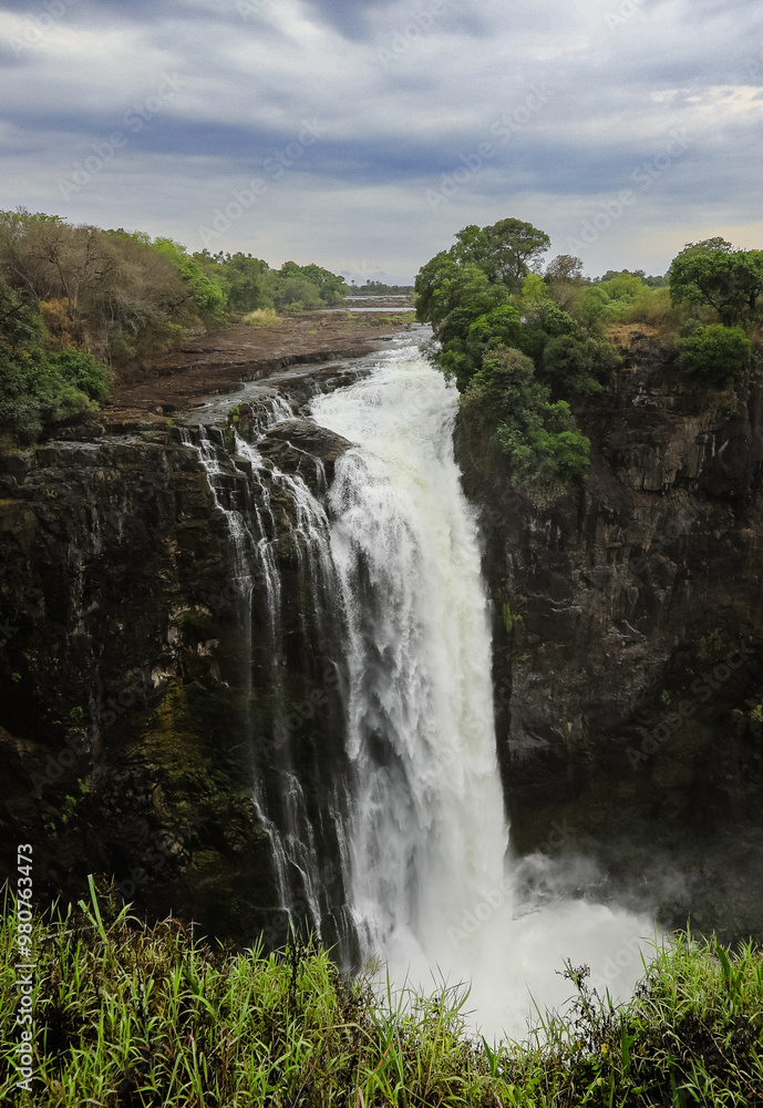 Fototapeta premium Majestic view of Victoria Falls cascading over cliffs in Zimbabwe during cloudy weather