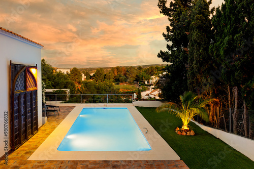 A blue pool illuminated by the golden color of the setting sun. You can see part of the cottage and the garden, as well as the sky illuminated by the setting sun.