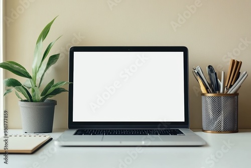 A laptop with a blank white screen on a minimalist desk, accompanied by a small potted plant, a notebook, and a pen holder, creating a clean and organized workspace atmosphere