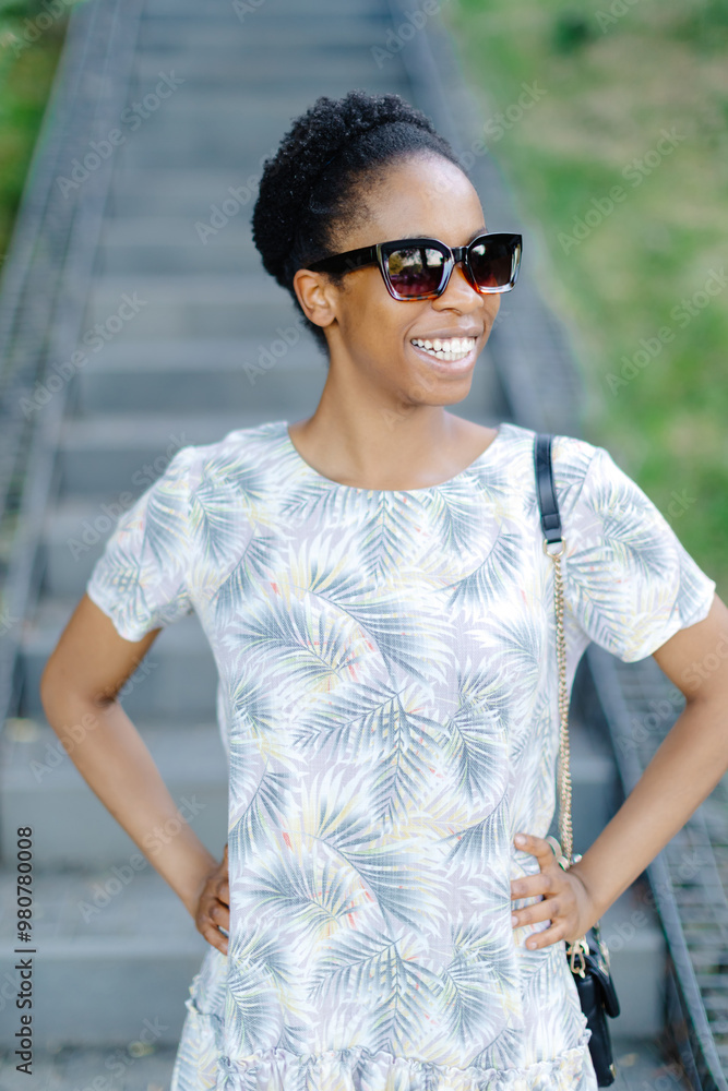 Dark-skinned lady laughs outside. Brunette curly woman in dress and sunglass smiles and walks outdoors Dark-skinned lady laughs outside. Brunette curly woman in dress and sunglass smiles and walks outdoors