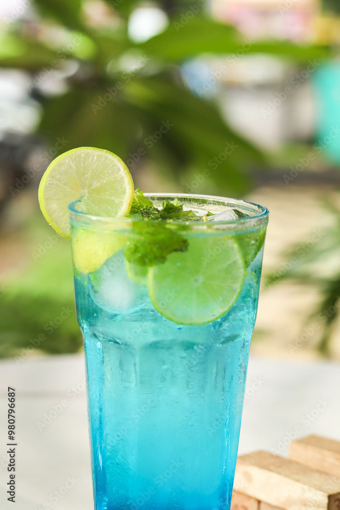 close up of Healthy Blue Lagoon Mojito soda served in glass with lemon and mint on a white table with jenga game and nature background. close up of Healthy Blue Lagoon Mojito soda served in glass with lemon and mint on a white table with jenga game and nature background.