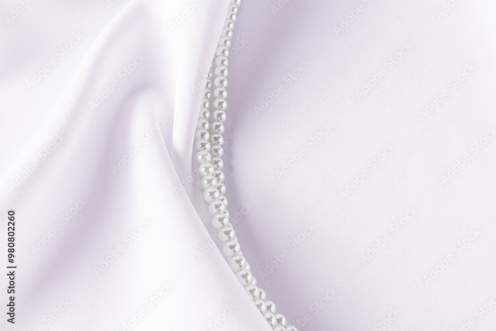 Beautiful delicate pearl beads on white satin fabric satin with chic soft folds. A copy space. wedding background. presentation of the accessory Beautiful delicate pearl beads on white satin fabric satin with chic soft folds. A copy space. wedding background. presentation of the accessory