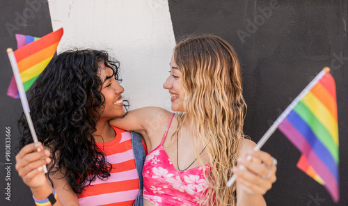 Multiracial lesbian couple celebrating with pride flags in park photo