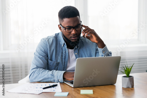 Concerned african american employee talking on mobile phone and looking at laptop screen, having issues with project, copy space