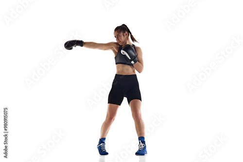 Jab punch. Full-length image of serious and concentrated young woman with sportive body, boxing athlete training isolated on white background. Concept of sport, hobby, active and healthy lifestyle