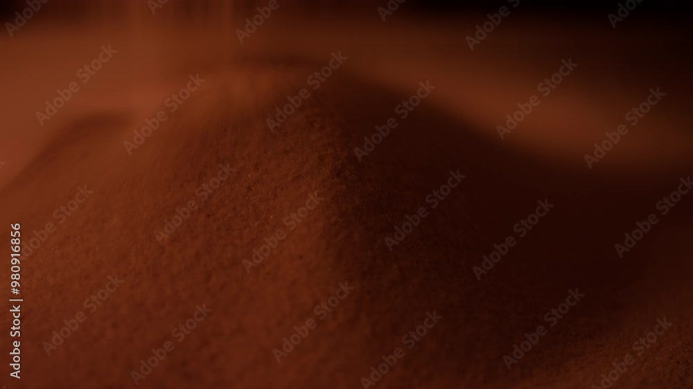 Close-up rack focus shot of small grains of sand falling from above making smooth mound in warm lighting Close-up rack focus shot of small grains of sand falling from above making smooth mound in warm lighting