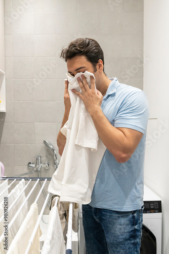 Young man sniffing clean laundry after washing	