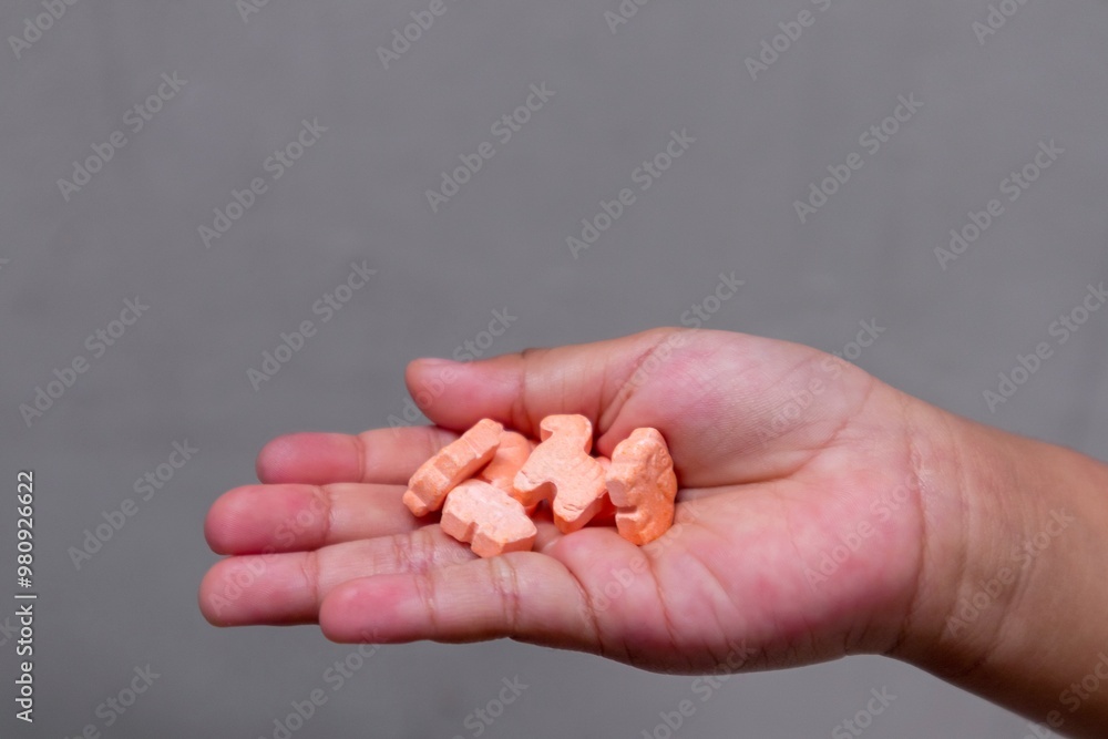 A child's hand holding a vitamin tablet in the shape of an animal character A child's hand holding a vitamin tablet in the shape of an animal character