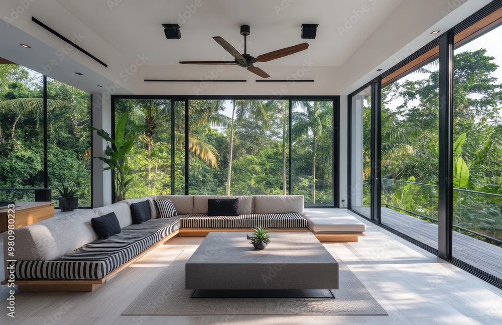 Modern living room interior with a large window and a tropical forest view, white walls, wooden floor, a grey sofa, a black coffee table, a ceiling fan Modern living room interior with a large window and a tropical forest view, white walls, wooden floor, a grey sofa, a black coffee table, a ceiling fan