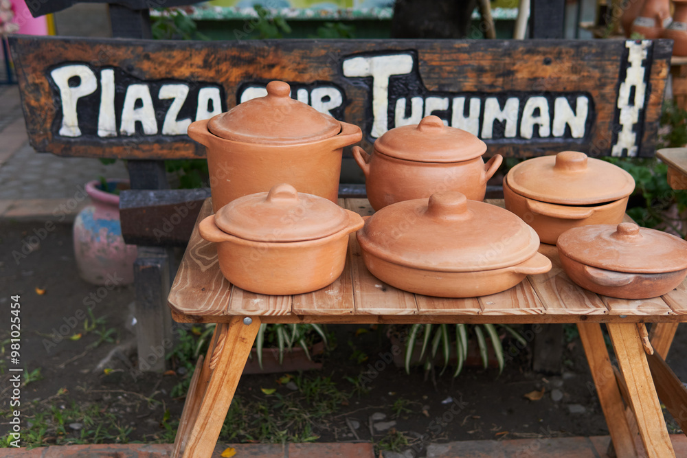Handmade earthenware pots with cover on from clay, rustic, for sale on a wooden table with a sign at the bottom that says tucuman square, in a fair. Handmade earthenware pots with cover on from clay, rustic, for sale on a wooden table with a sign at the bottom that says tucuman square, in a fair.