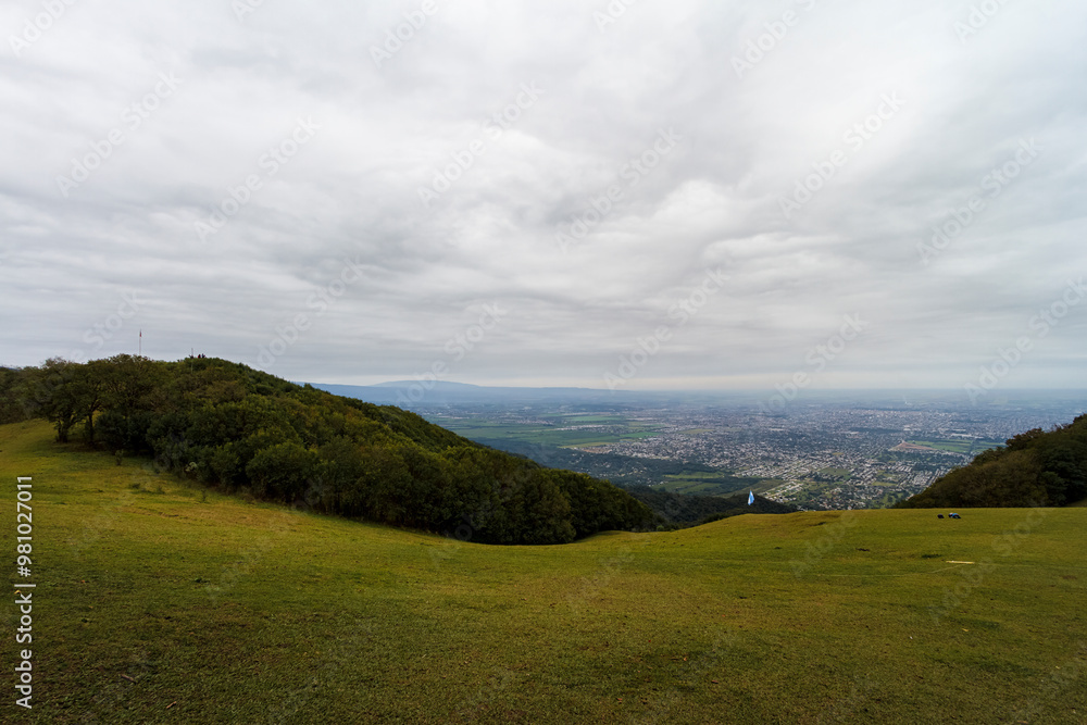 Grass prairie with Argentine flag and city of San Miguel de Tucumán in the background Grass prairie with Argentine flag and city of San Miguel de Tucumán in the background