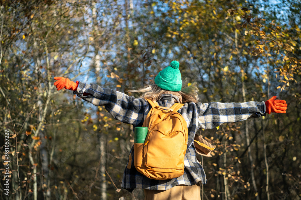 Naklejka premium Contented woman traveler having good time outside, enjoying wandering in autumn forest. Female tourist backpacker scrolling in sunny fall weather outside. Nature therapy, stress free, break from city