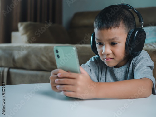 Cute elementary school boy wearing headphones holding a smartphone. Boy studying online on smartphone or homeschooling, listening to music or playing games, Concept of online learning via smartphone. photo