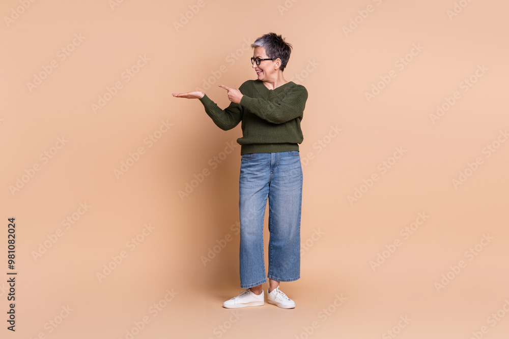 Photo of cheerful senior lady wear green stylish clothes demonstrate empty space offer isolated on beige color background Photo of cheerful senior lady wear green stylish clothes demonstrate empty space offer isolated on beige color background