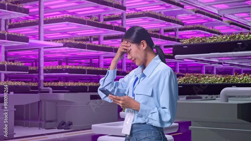 Side View Of An Asian Female Professional Worker Standing With Her Smartphone In Vertical Farm, High-tech Industrial Facility, Checking With Dissapionted And Nodding Her Shead  photo