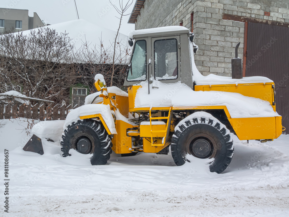 A bulldozer for clearing roads of snow during a snowfall. A bulldozer with large wheels for road construction works stands in a snowdrift in winter. Road equipment. A bulldozer for clearing roads of snow during a snowfall. A bulldozer with large wheels for road construction works stands in a snowdrift in winter. Road equipment.