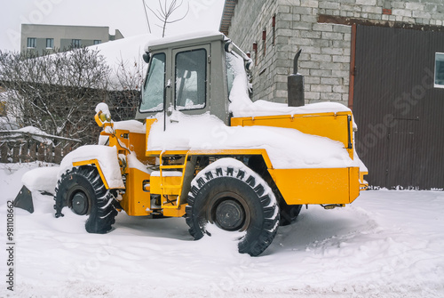 A bulldozer for clearing roads of snow during a snowfall. A bulldozer with large wheels for road construction works stands in a snowdrift in winter. Road equipment.