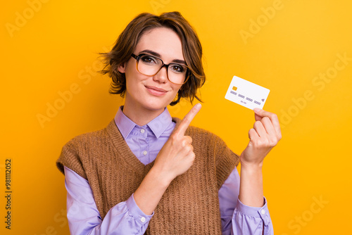 Portrait of positive woman with bob hairdo wear knit waistcoat indicating at credit card in hand isolated on yellow color background photo