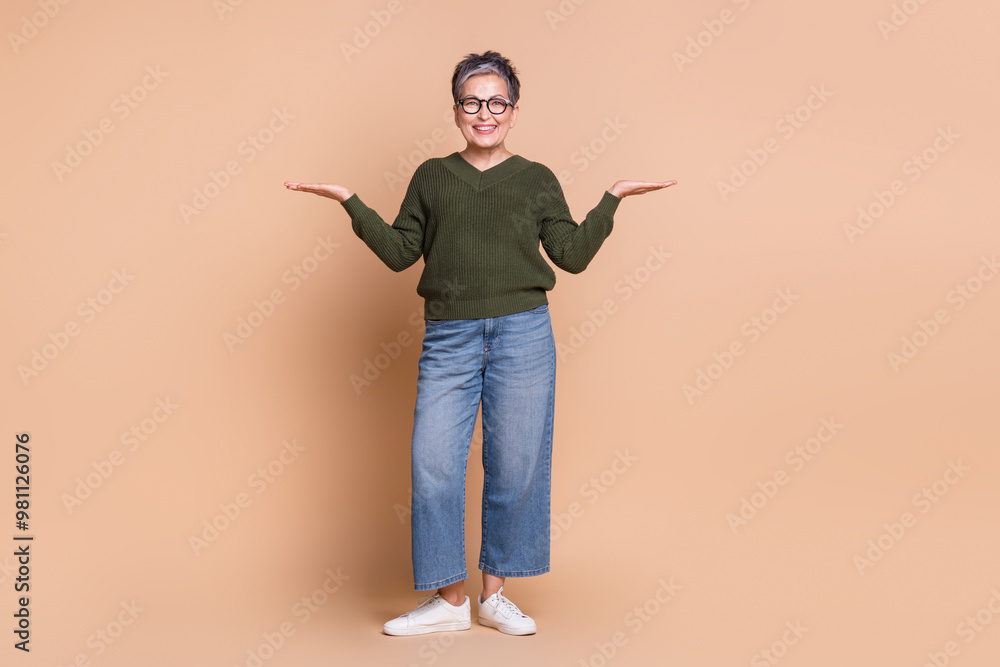 Photo of charming pretty nice mature woman wear green stylish clothes hold empty space isolated on beige color background Photo of charming pretty nice mature woman wear green stylish clothes hold empty space isolated on beige color background