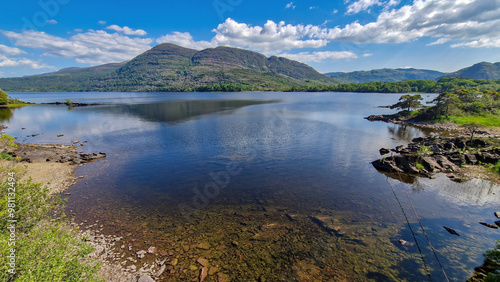 A breathtaking view of Muckross Lake, where the shimmering waters reflect the vibrant colors of the surrounding landscape, inviting visitors to immerse themselves in the serene beauty of nature.