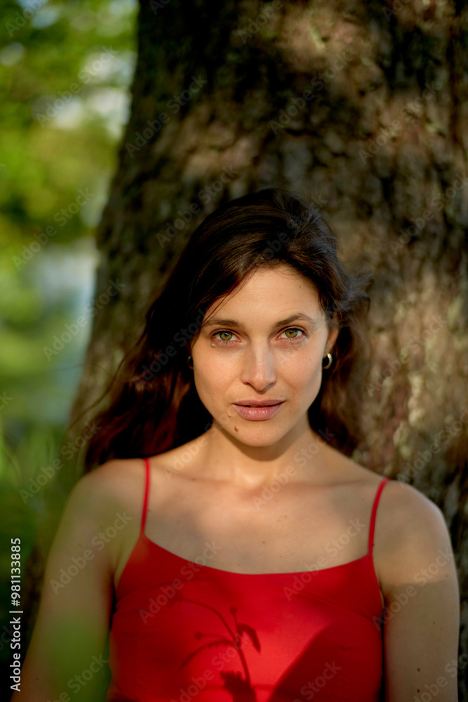 Woman in red dress standing in front of a tree with sunlight filtering through the leaves. Woman in red dress standing in front of a tree with sunlight filtering through the leaves.