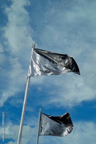 Two black flags flutter against a backdrop of a blue sky with scattered clouds. photo