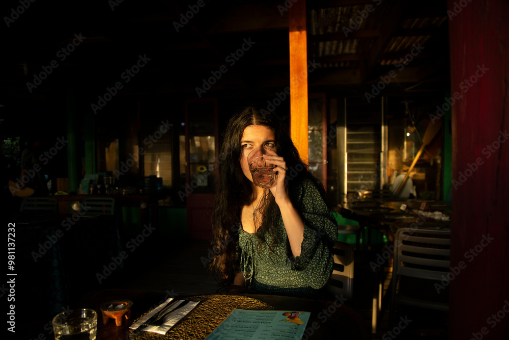 Woman having a drink in a restaurant at sunset with sunlight illuminating her face, Titikaveka, Rarotonga, Cook Islands Woman having a drink in a restaurant at sunset with sunlight illuminating her face, Titikaveka, Rarotonga, Cook Islands