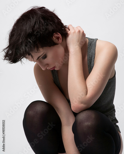 Young adult with short hair sitting in a crouched position, holding their shoulder, against a white background. photo