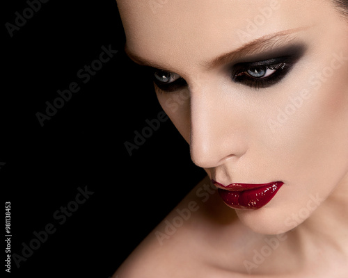 Close-up of a woman with dramatic makeup featuring smoky eyes and glossy red lips against a black background. photo