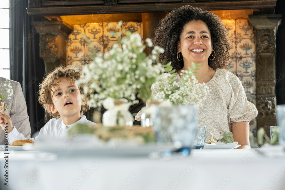 A smiling woman and a young child are seated at a table beautifully decorated with flowers. A smiling woman and a young child are seated at a table beautifully decorated with flowers.