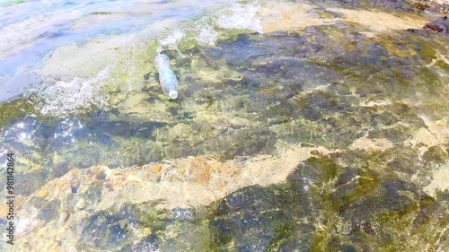 Plastic bottle washed up on the shore. Disposable plastic waste pollutes the beach. Marine pollution caused by human. Poor trash management affects the environment. Long-lasting ecological problem.