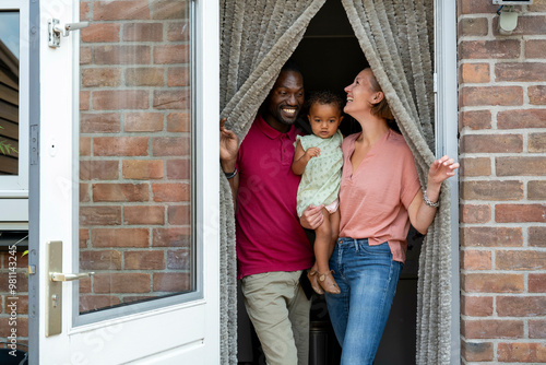 Family smiling and standing at the entrance of their brick home behind an open door. photo