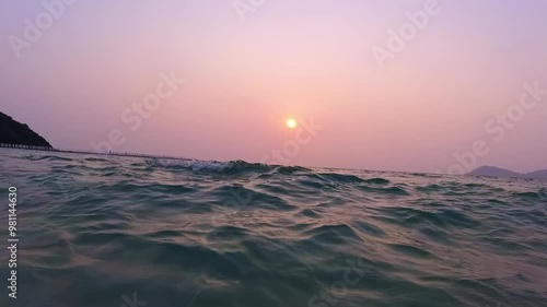 POV beautiful sunset with pink sky while surfing through the waves in the ocean. Outdoor active lifestyle on summer holidays. Vacation beach trip at the seaside. Travel advertising.