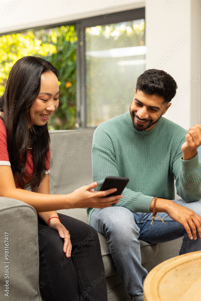 Smiling diverse friends sitting on couch, looking at smartphone and chatting together Smiling diverse friends sitting on couch, looking at smartphone and chatting together