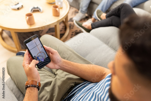 Using smartphone, man relaxing on couch with friends in living room