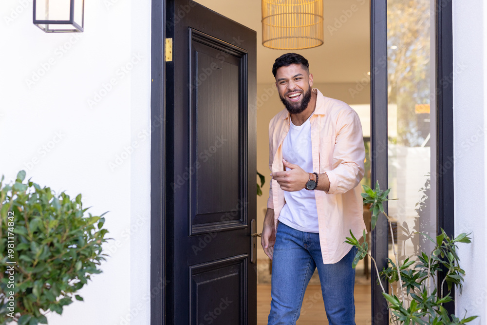 Obraz premium Smiling man welcoming friends at front door, standing in doorway of home, copy space